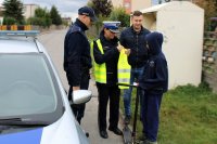 policjanci wraz z pracownikiem UG w Miedźnie wręczają chłopcu z hulajnogą odblaski i lampki rowerowe