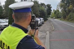 Zdjęcie przedstawia policjanta ruchu drogowego, który mierzy prędkość nadjeżdżającego pojazdu.