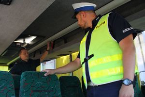 umundurowany policjant wraz inspektorem transportu drogowego kontrolują wnętrze autobusu