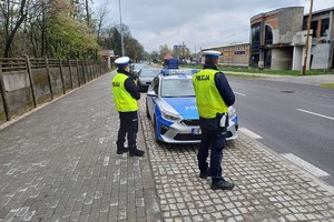 umundurowani policjanci stoją przy radiowozie zaparkowanym przy drodze